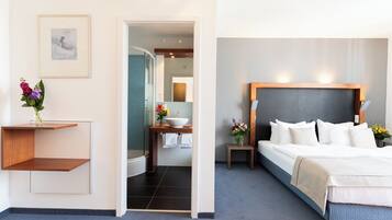 Una habitación de hotel con cama, mesita de noche y baño con lavabo y ducha.