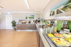 A buffet setup with various food items, a potted plant, and a painting on the wall. - Hotel Aviva (Leipzig)