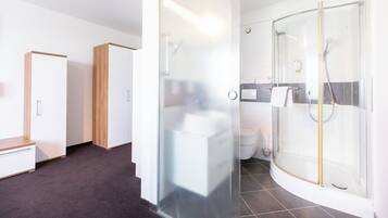 A modern bathroom with a glass-enclosed shower, a toilet, and a wooden wardrobe.