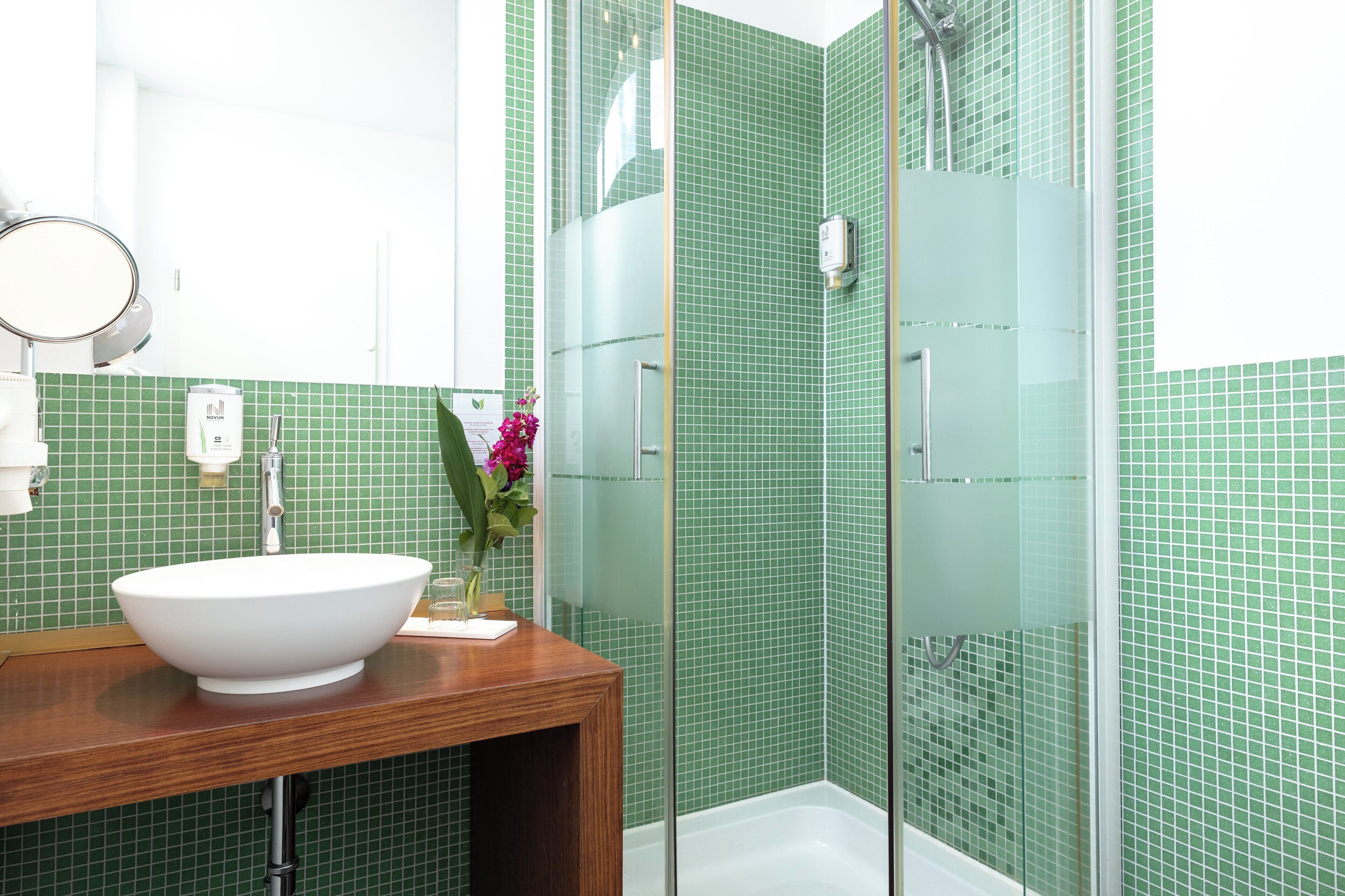 A bathroom with a white sink, a mirror, and a shower with green tiles.