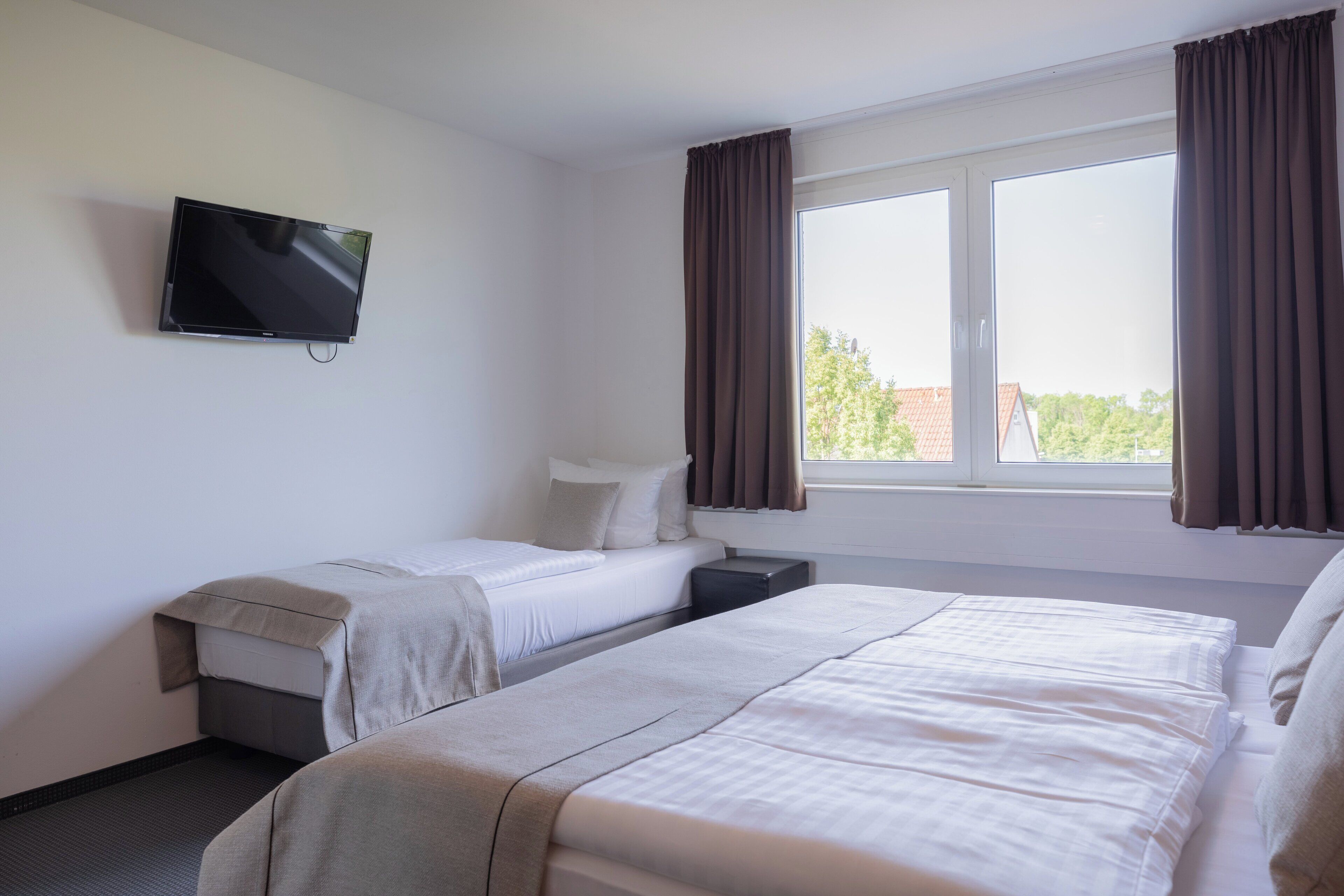 A hotel room with two beds, a TV mounted on the wall, and a large window with curtains.