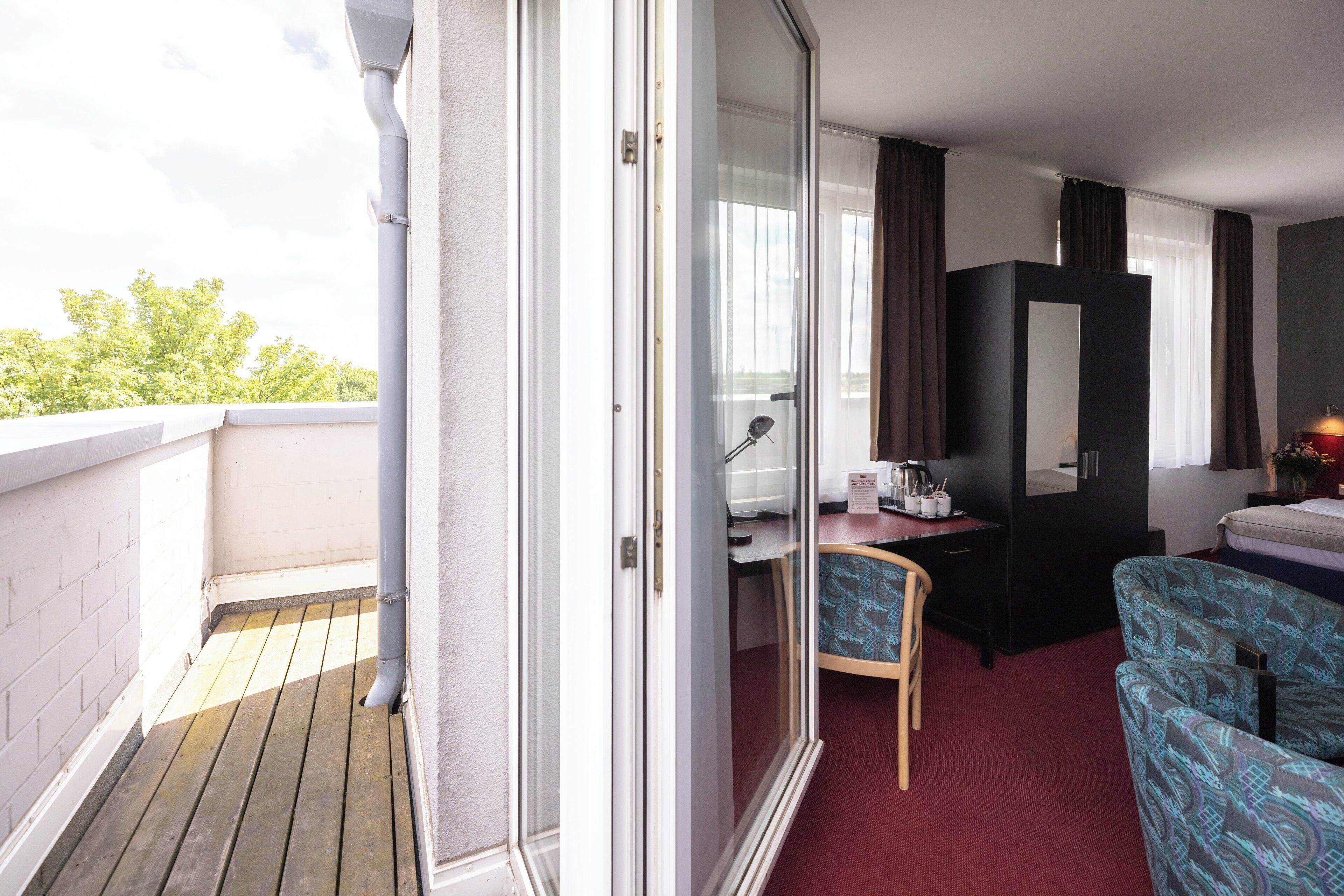 A hotel room with a balcony, a bed, a desk, and a chair.