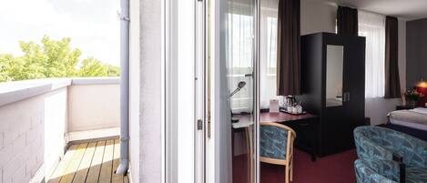 A hotel room with a balcony, a bed, a desk, and a chair.