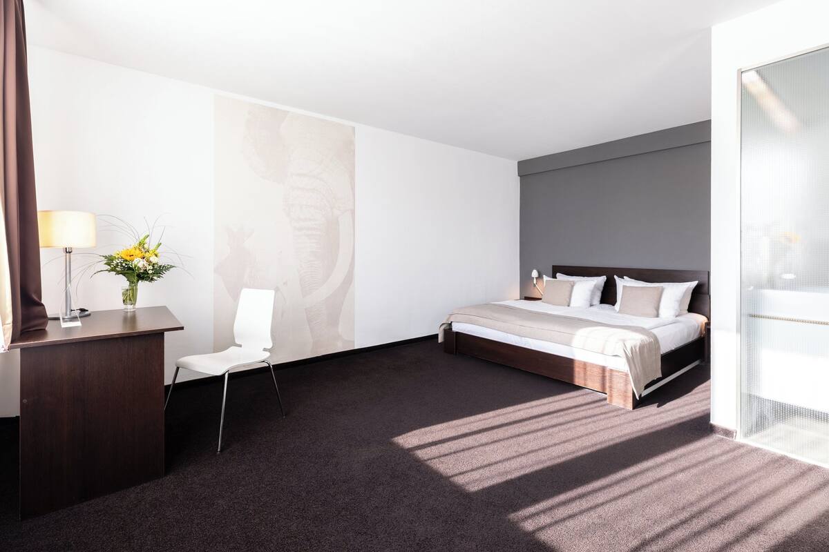 A modern hotel room with a bed, a desk, a chair, and a desk lamp.