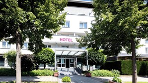 A hotel entrance with a covered walkway, potted plants, and a clear view of the building's facade. - Hotel Aviva (Leipzig)