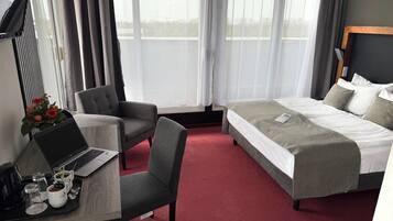 A hotel room with a bed, a desk with a laptop, a chair, and a dining area with a tray of food and drinks.