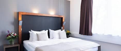 A hotel room with a large bed, a nightstand with a vase of flowers, and a window with curtains.