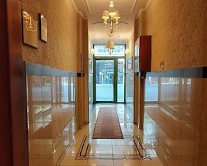 A hotel lobby with a marble floor, a central chandelier, and framed artwork on the walls. - Alexandria Hotel (Thessaloniki)