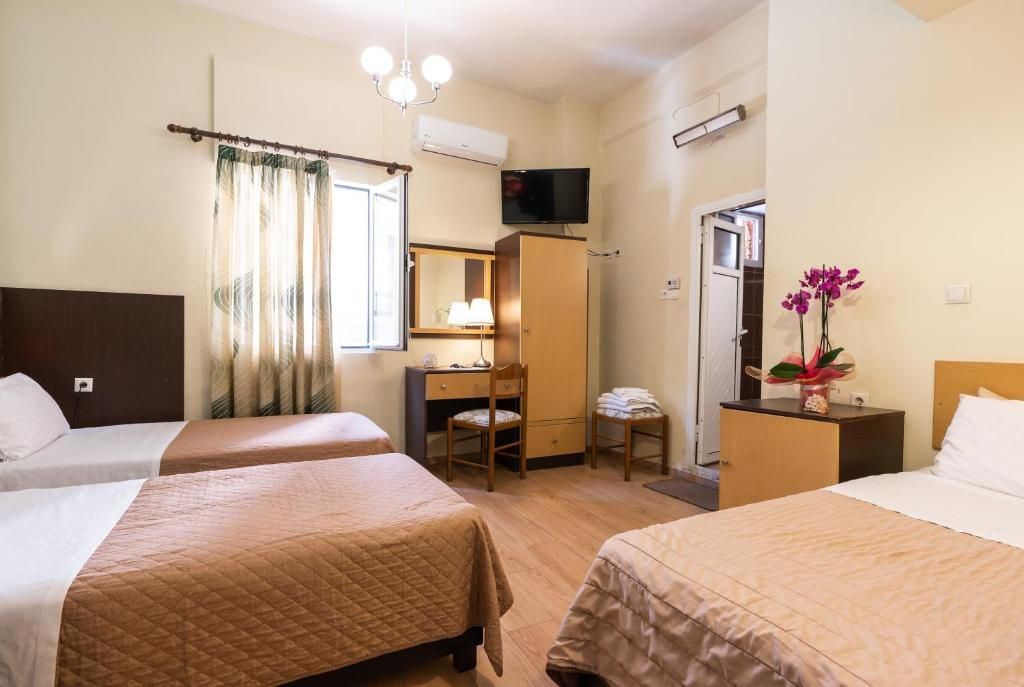 Une chambre d’hôtel avec deux lits, un bureau, une chaise, une télévision et une petite table sur laquelle est posé un vase de fleurs.
