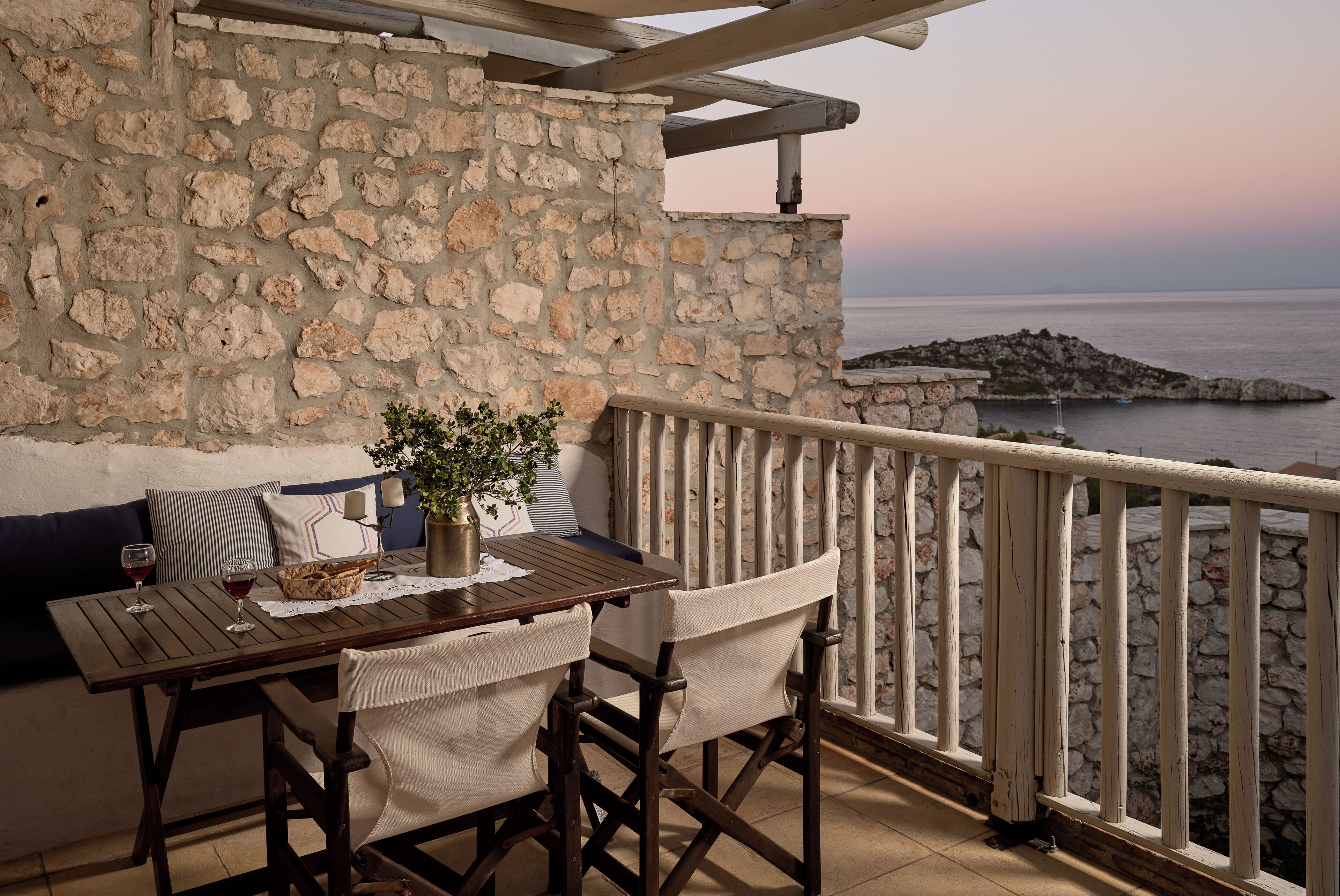 A stone wall with a wooden table and chairs, a potted plant, and a view of the sea.