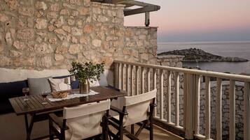 A stone wall with a wooden table and chairs, a potted plant, and a view of the sea.