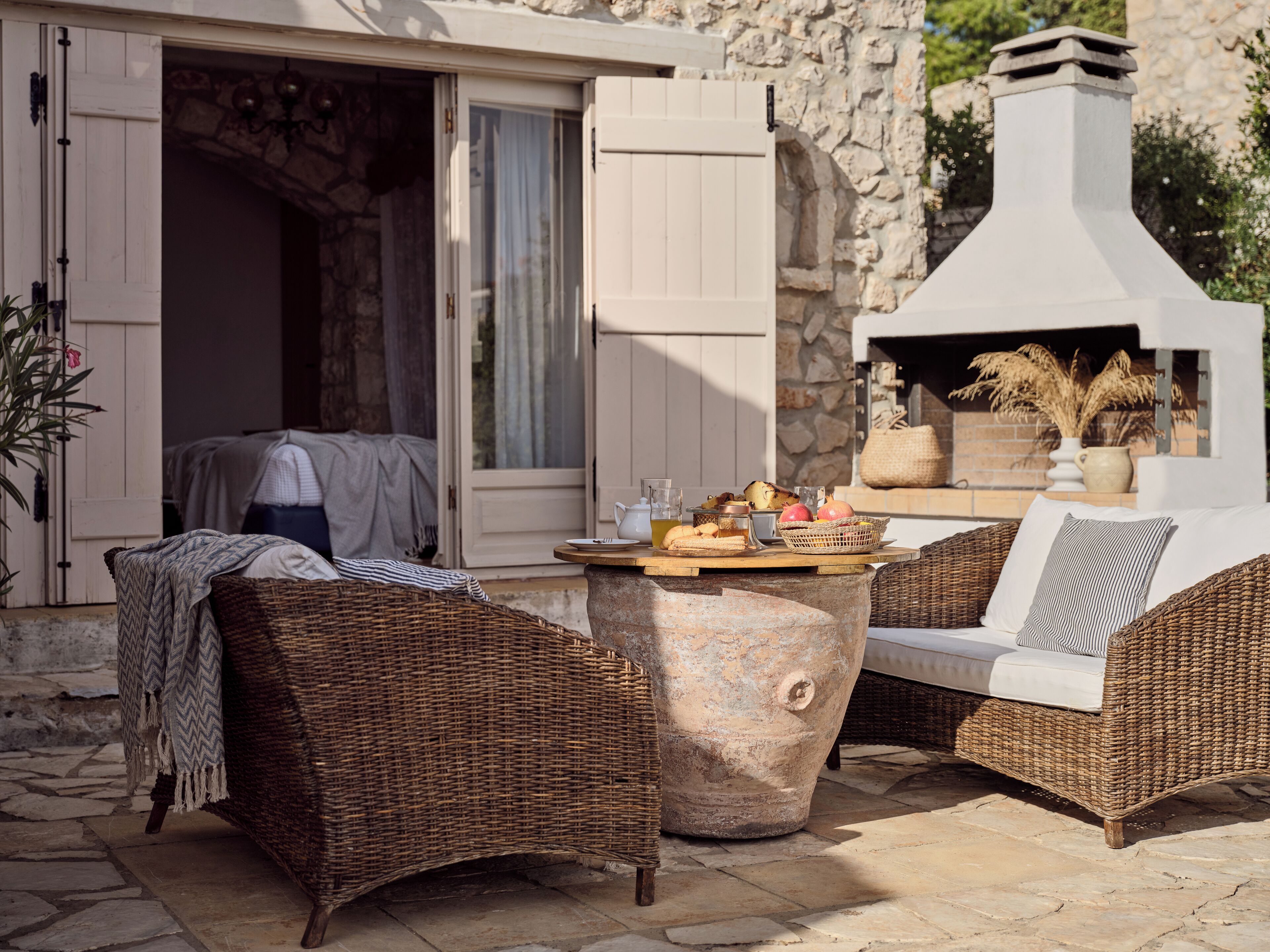An outdoor seating area with wicker furniture, a stone table, and a stone fireplace.