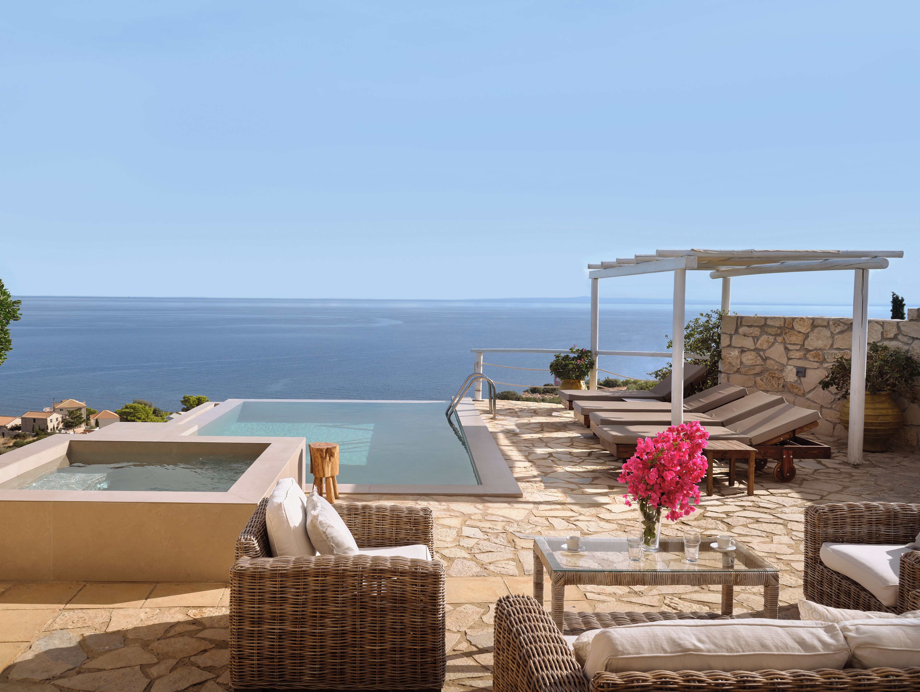 Piscina infinita en la azotea con sillones de descanso y una pérgola con vistas al mar.