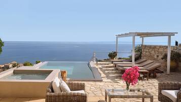 Piscina infinita en la azotea con sillones de descanso y una pérgola con vistas al mar.