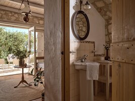 Un baño con pared de piedra, puerta de madera, lavabo con toalla y espejo.