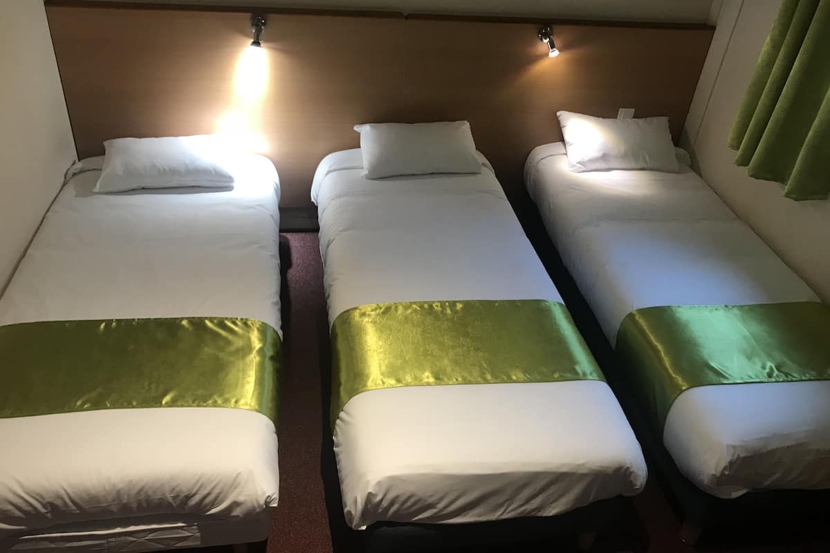 A hotel room with three single beds, each with white bedding and a green accent.