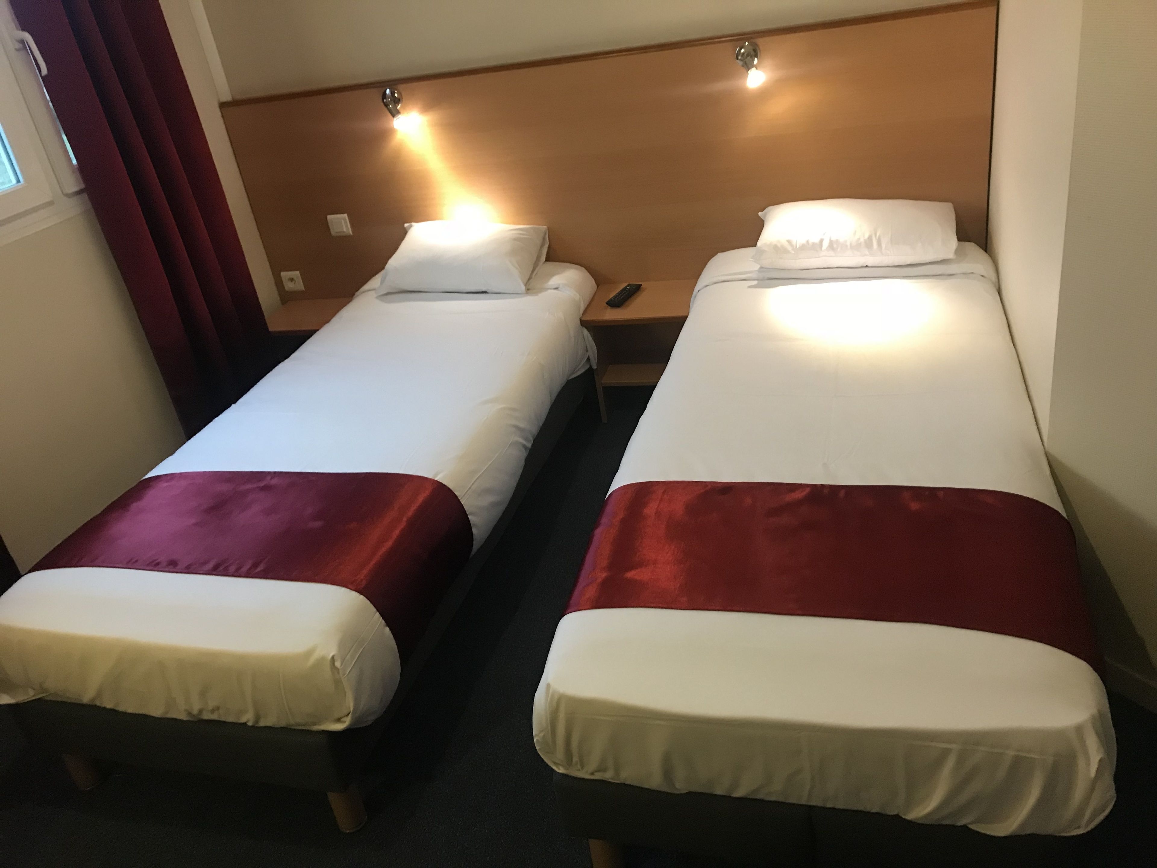 Duas camas de solteiro com cabeceiras, uma mesa de cabeceira e uma cortina vermelha.