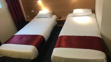 Duas camas de solteiro com cabeceiras, uma mesa de cabeceira e uma cortina vermelha.