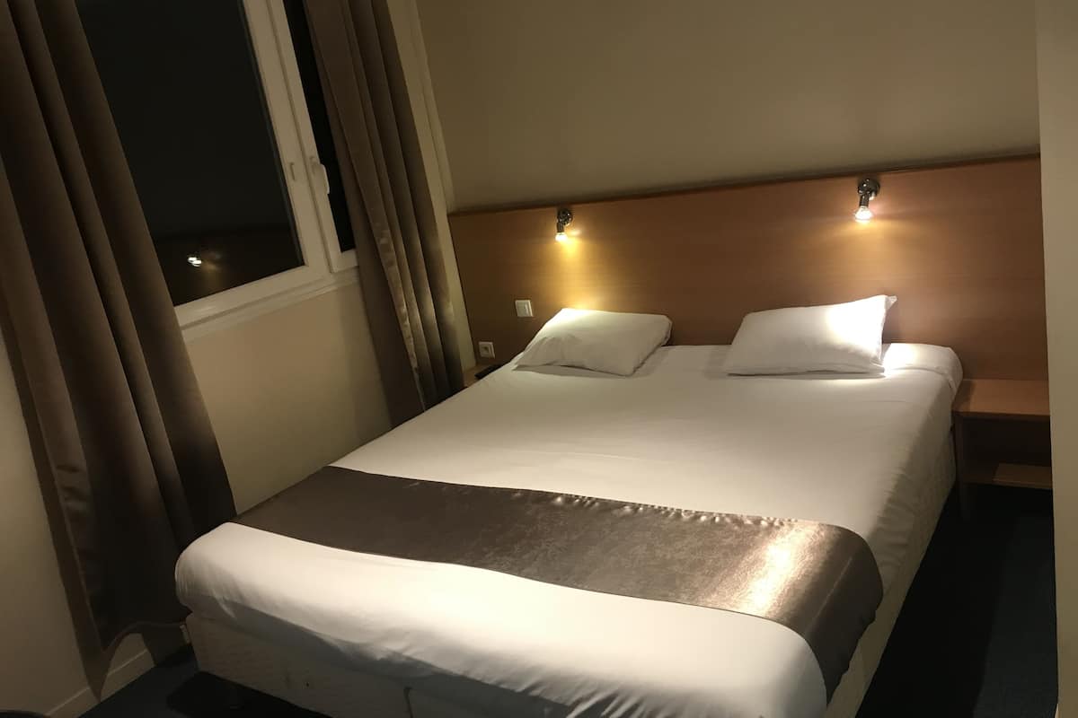 A hotel room with a bed, curtains, a nightstand, and wall-mounted lights.