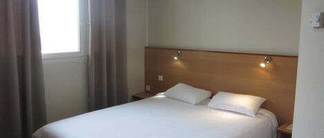 Une chambre d’hôtel avec un grand lit, deux tables de chevet, une tête de lit dotée d’un éclairage intégré et une fenêtre avec des rideaux.