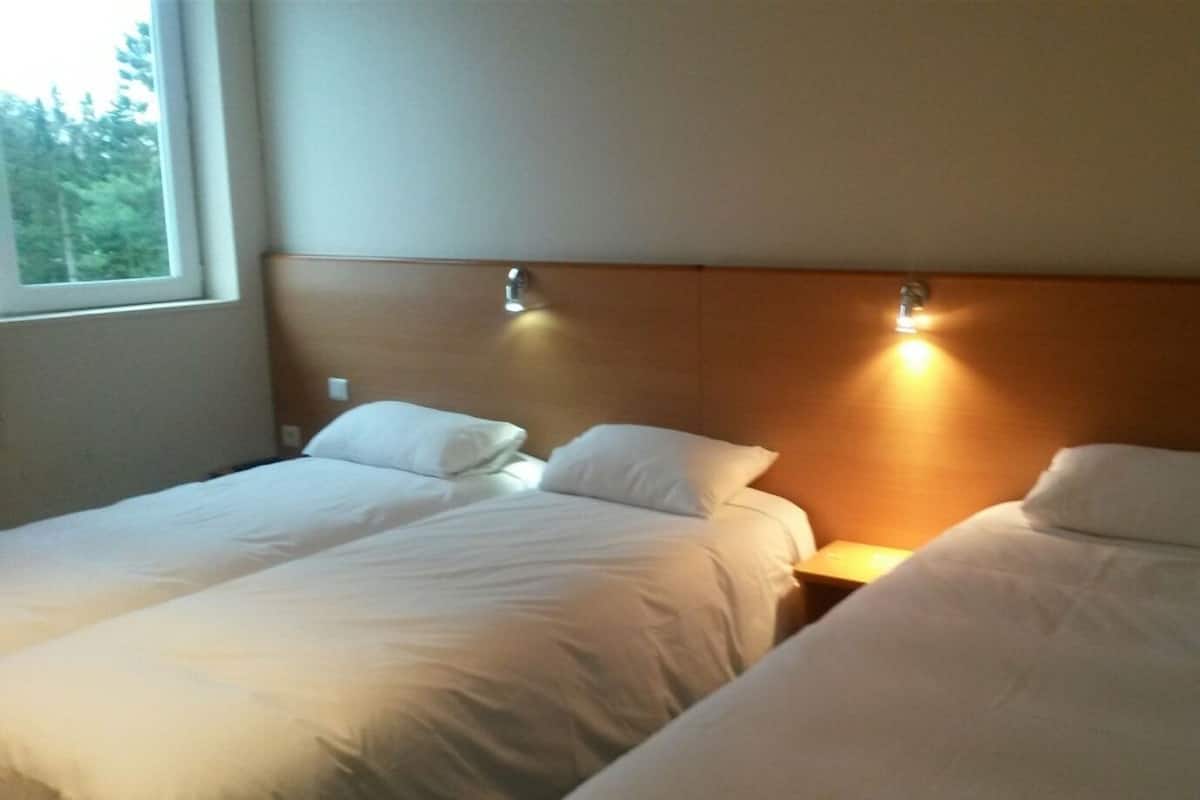 A hotel room with two single beds, a wooden headboard, bedside lamps, and a window with a view of trees.