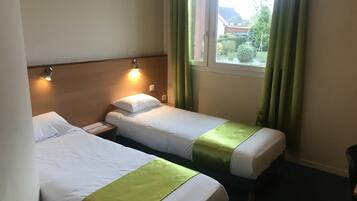 A hotel room with two single beds, a nightstand, a window with curtains, and a view of the outside.