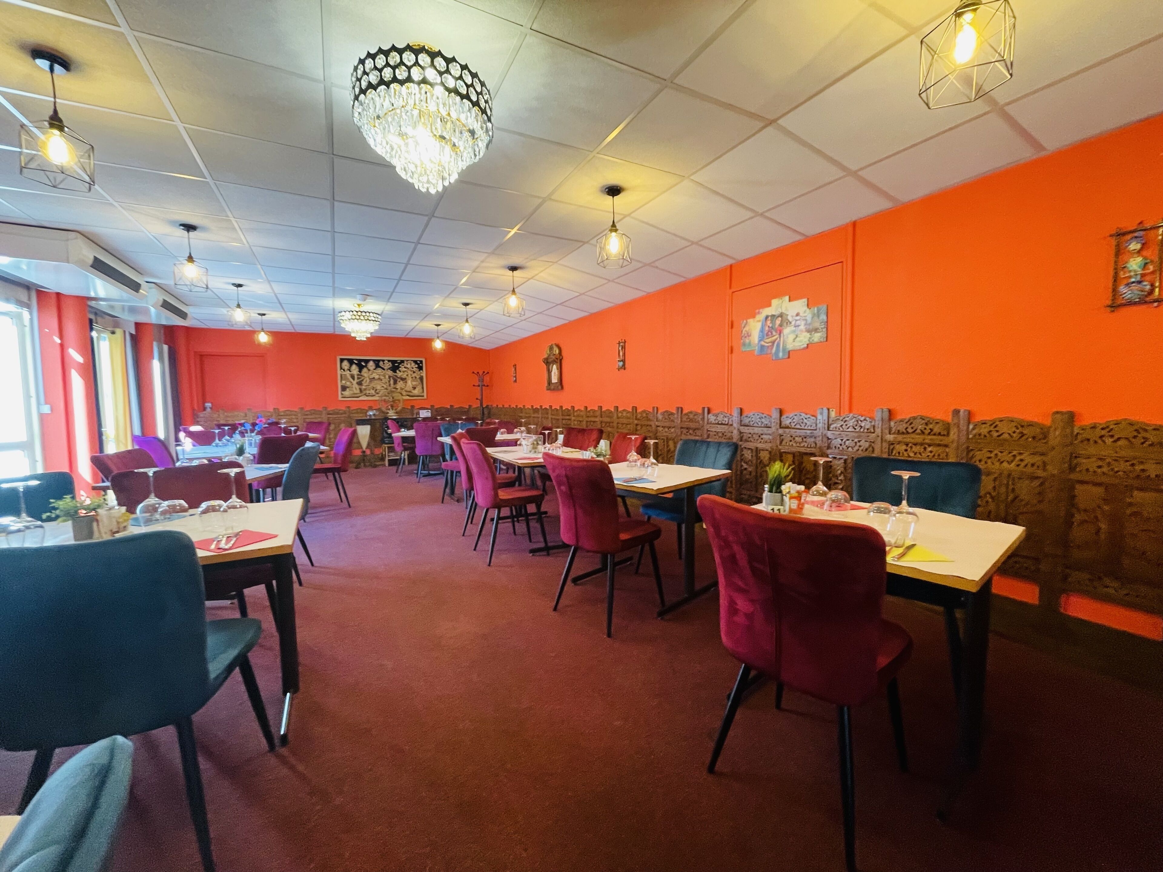 A restaurant with multiple tables and chairs, a chandelier, and orange walls.