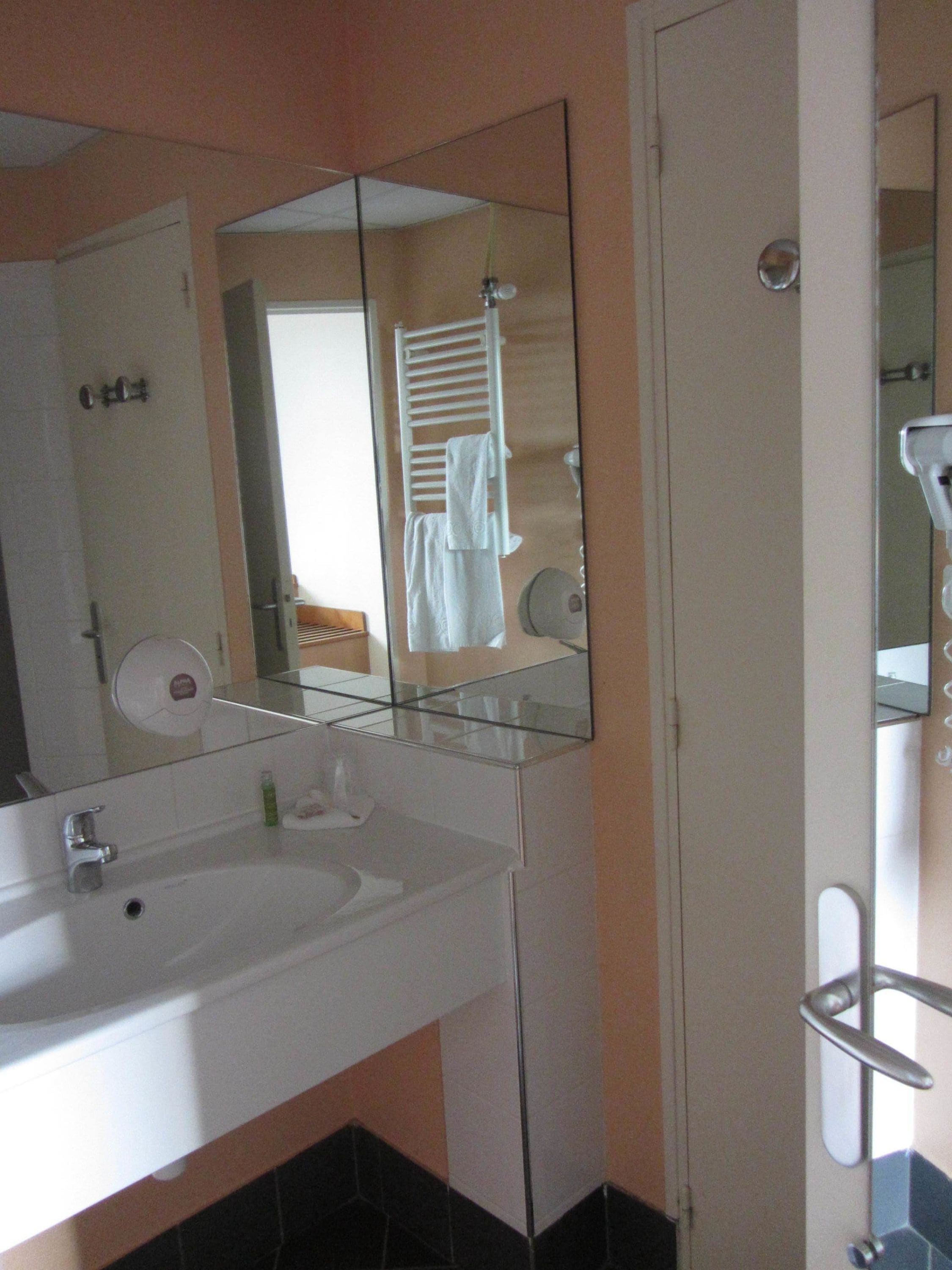 A bathroom with a glass-enclosed sink, a towel rack, and a mirror reflecting a towel hanging on the rack.