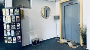Un espace d’accueil avec une étagère présentant des boîtes de jeux, un miroir rond, une porte dotée d’un écran numérique et une petite plante.