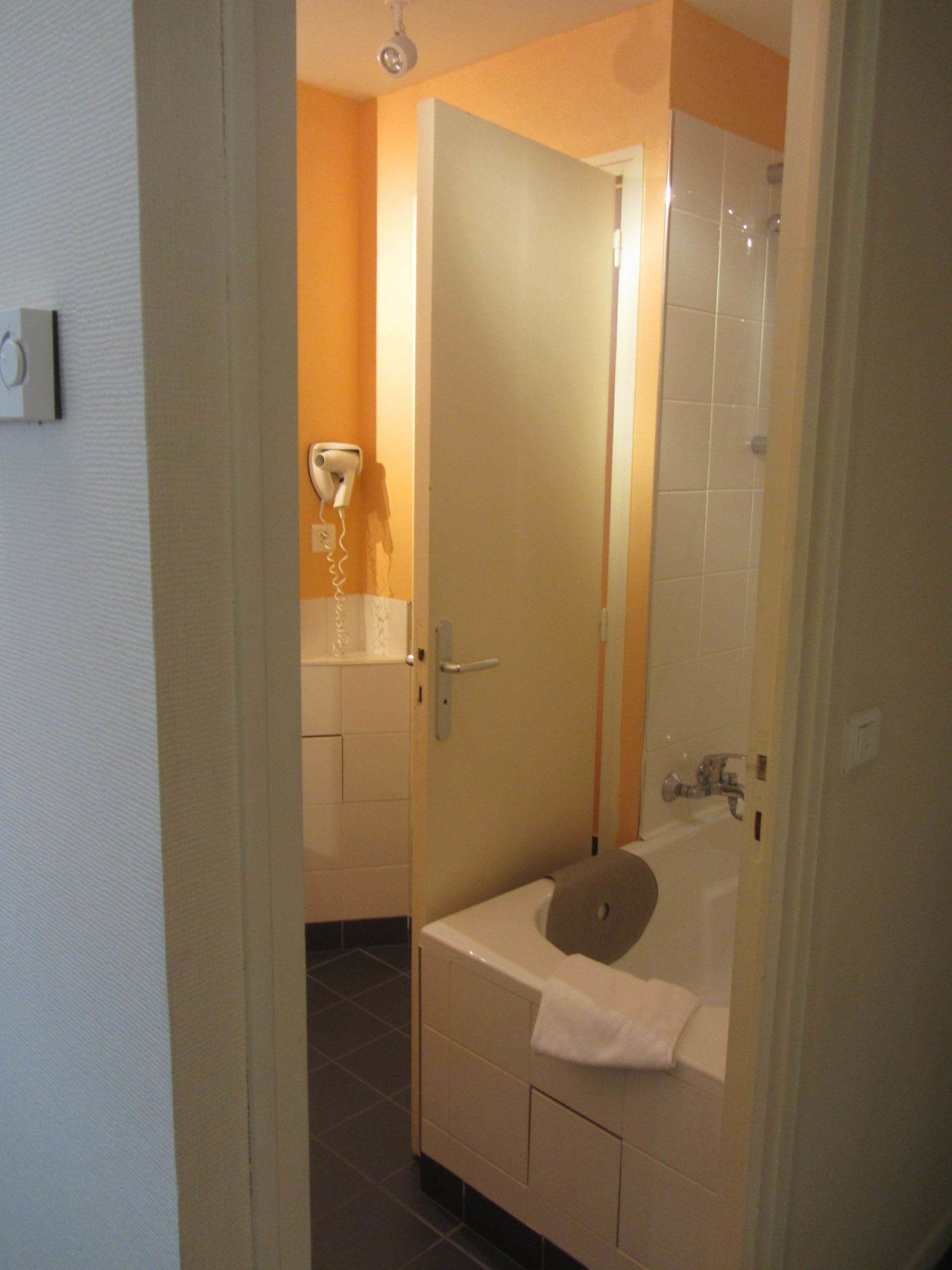 A bathroom with a bathtub, a towel, and a hairdryer on the wall.