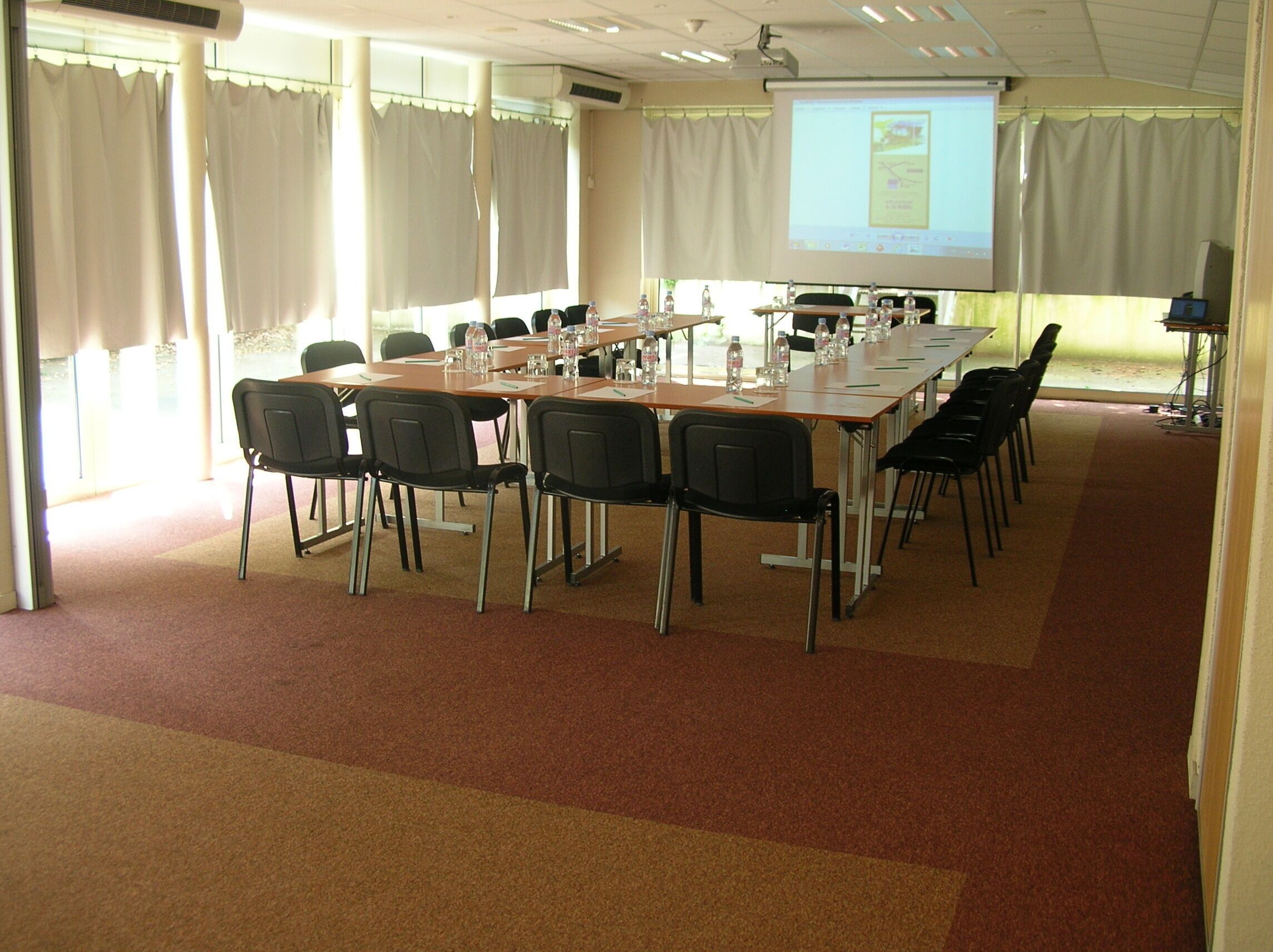 A conference room with a long table, chairs, a projector screen, and a presentation.