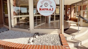 L’entrée d’un restaurant avec une façade en verre, un mur en pierre et une enseigne indiquant « Natraj, restaurant indien ».