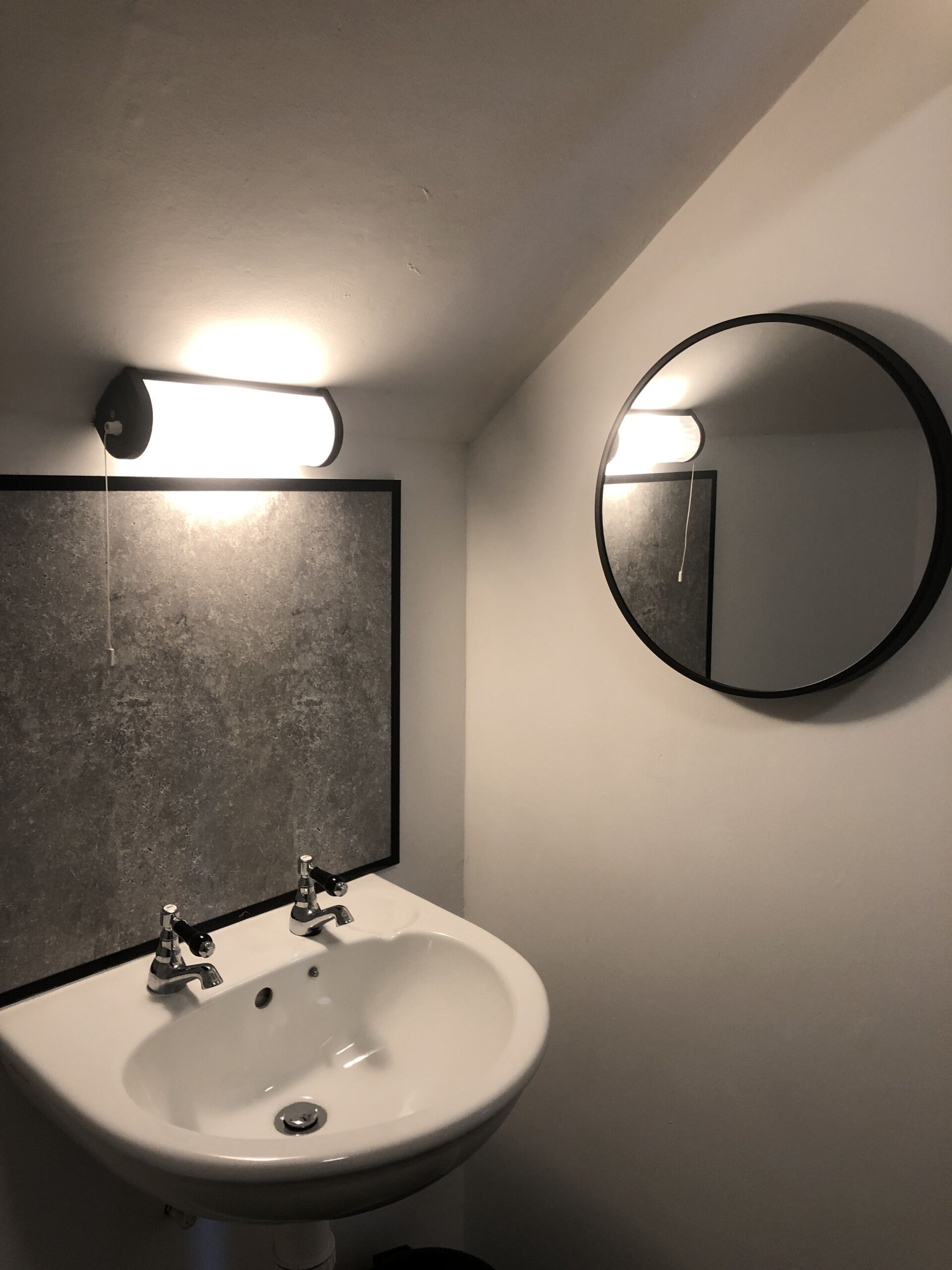 A bathroom with a white sink, a rectangular mirror with a black frame, and a round mirror.