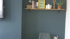 Una sala moderna con una pared azul oscuro, dos sillones grises, una mesa blanca y un estante de madera con objetos decorativos.