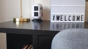 Un bureau avec une lampe, une multiprise, un panneau d’accueil et des livres.