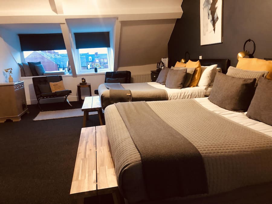 Una habitació d'hotel moderna amb dos llits, una taula petita, una cadira i vista a la ciutat a través de grans finestres.