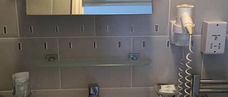 A bathroom with a white sink, a mirror, and a hairdryer on a wall-mounted charging station.