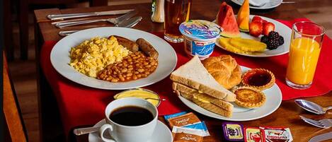 Una mesa de desayuno con platos de huevos, frijoles, tostadas y pasteles, una taza de café y un vaso de jugo de naranja.