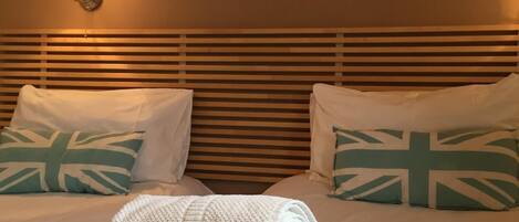 Ein Hotelzimmer mit einem Bett, Kissen mit Union-Jack-Motiven, einem Gemälde mit roten Blumen und einer Wandlampe.