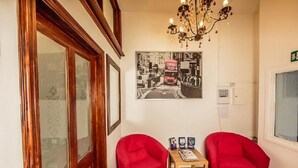Una habitación con dos sillas rojas, una mesa de madera con revistas, un candelabro y una fotografía blanco y negro en la pared.