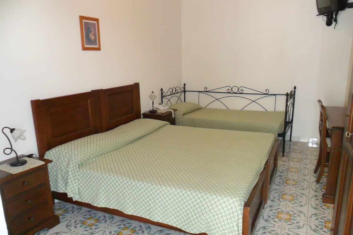 Une chambre avec deux lits simples, une table de chevet en bois avec une lampe, une commode et un téléviseur fixé au mur.