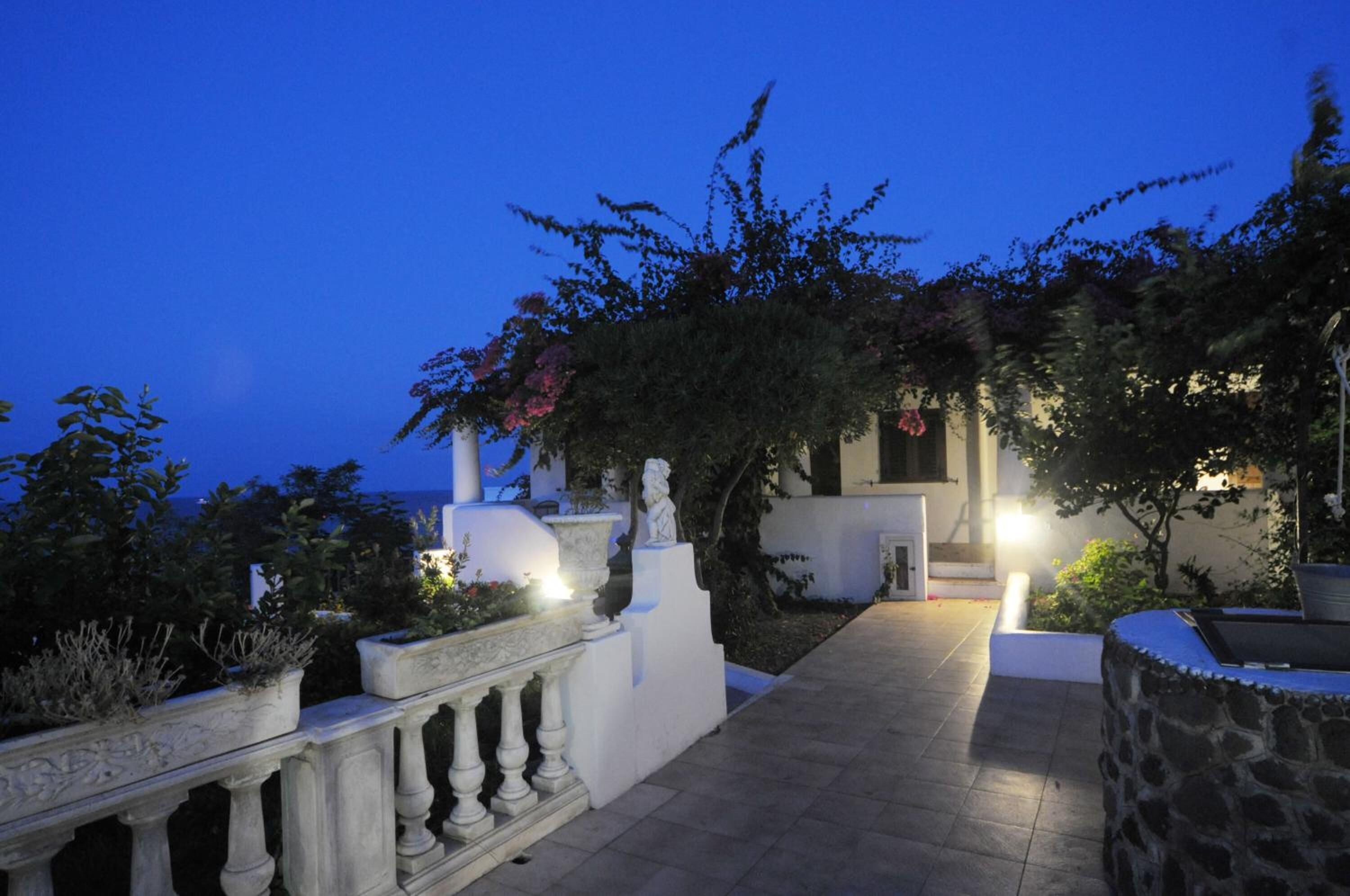 A well-lit pathway leading to a building with a white facade and a stone balustrade.