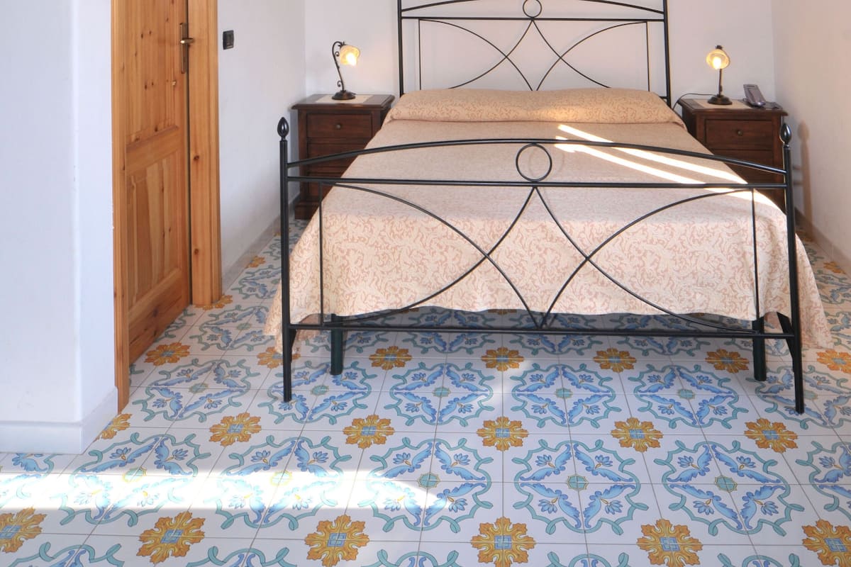 Une chambre avec un plafond en bois, un lit avec un cadre en métal, deux tables de chevet avec des lampes et une porte.