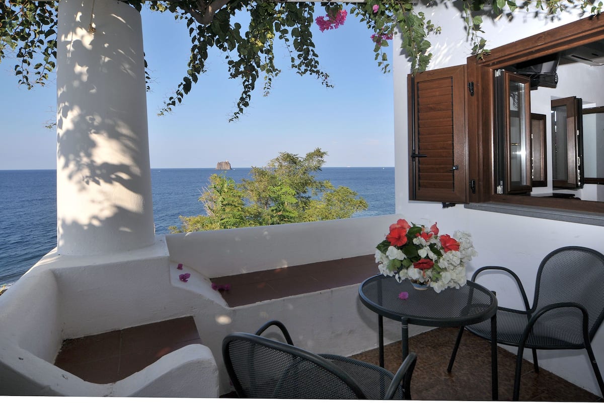 Un balcon orné d’une colonne blanche, une table avec des chaises et un vase de fleurs.
