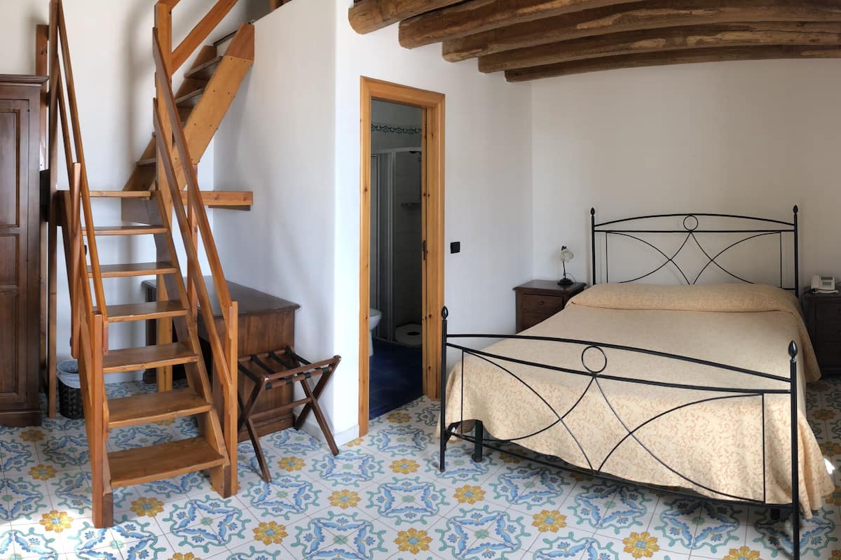 Une chambre avec une échelle en bois, un lit, une table de chevet et une armoire.