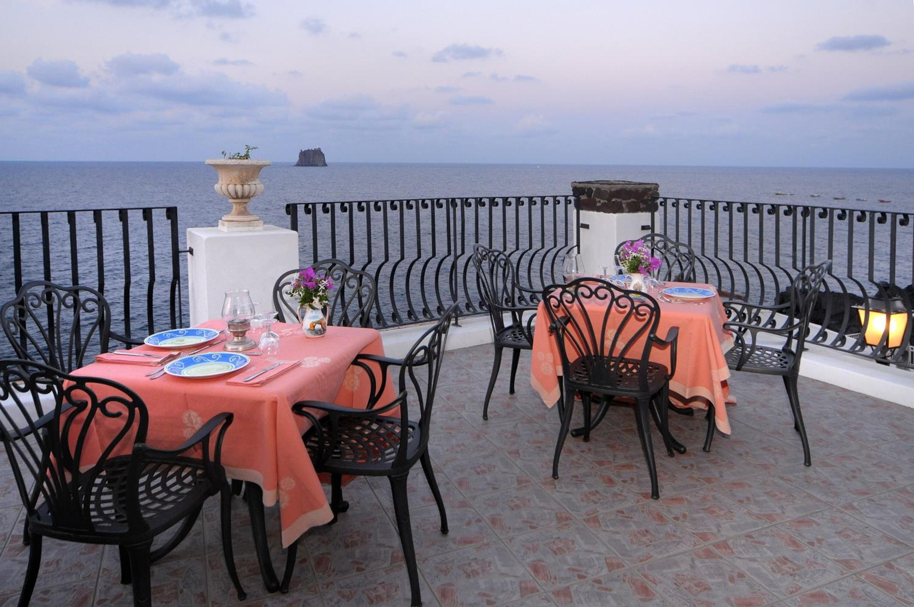 Una terraza con mesas y sillas, vista al mar y un jarro decorativo.