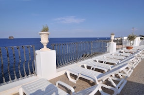 Een terras aan zee met witte lounge stoelen en een hekwerk met uitzicht op de oceaan.