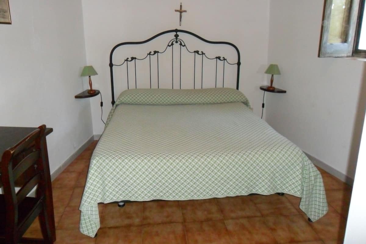 Un lit simple avec une croix sur la tête de lit, deux tables de chevet avec des lampes et une chaise en bois.