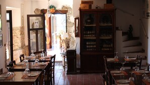 Un comedor con varias mesas dispuestas para el servicio, un mueble grande de madera con puertas de cristal y una pared de piedra.