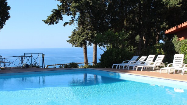 Una piscina azul clara con sillas de descanso blancas y vista al mar.
